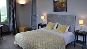 A hotel room with a bed, two bedside tables with lamps, a painting on the wall, and a window with curtains.
