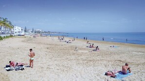 A wide sandy beach with people sunbathing and swimming.