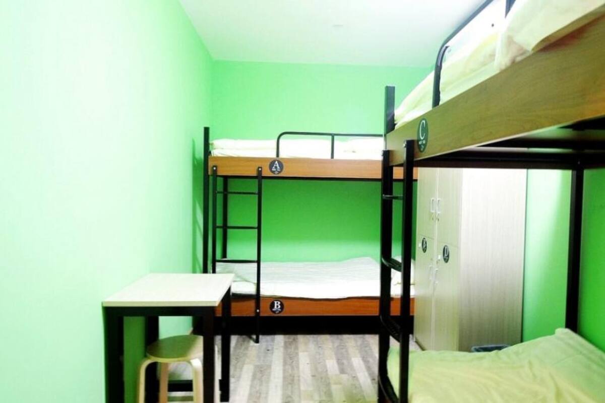 Une chambre avec un lit superposé, un bureau et une chaise, des murs verts et une porte.