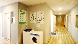 Een hotelgang met een houten vloer, een wasmachine en informatieposters op de muren.