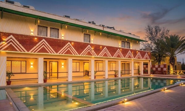 Un hotel con piscina, varias habitaciones con ventanas y techo verde.