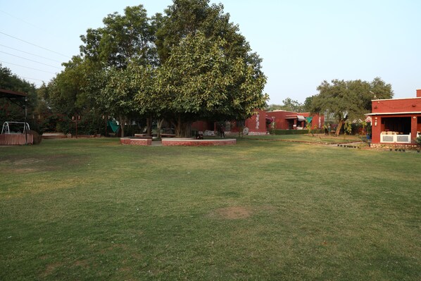 A spacious outdoor area with a large lawn, a swing set, and a brick building with a covered area.