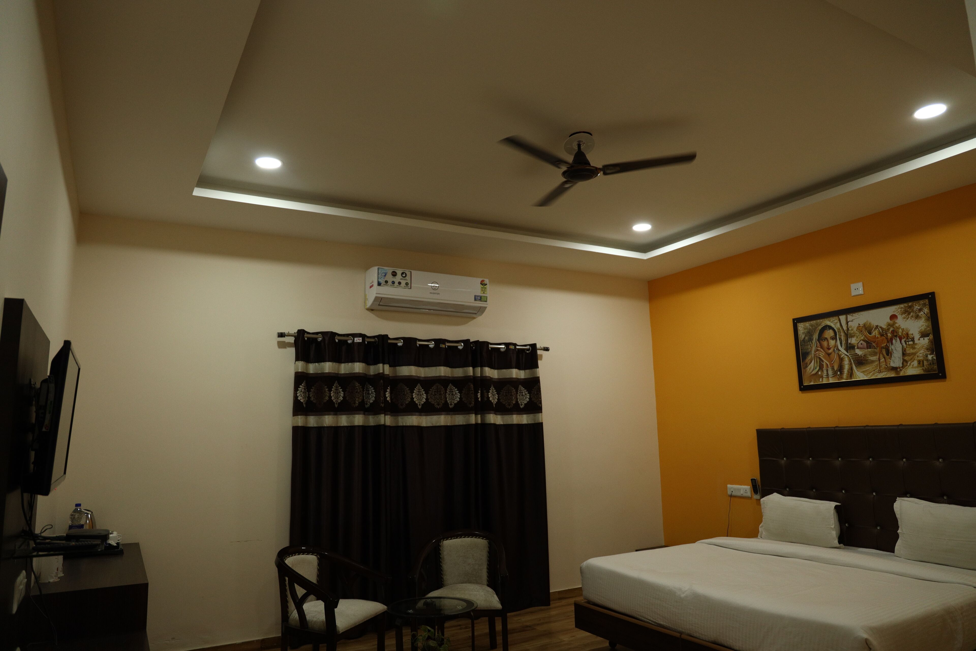 Una habitación de hotel con cama, escritorio, silla, ventilador de techo y aire acondicionado.