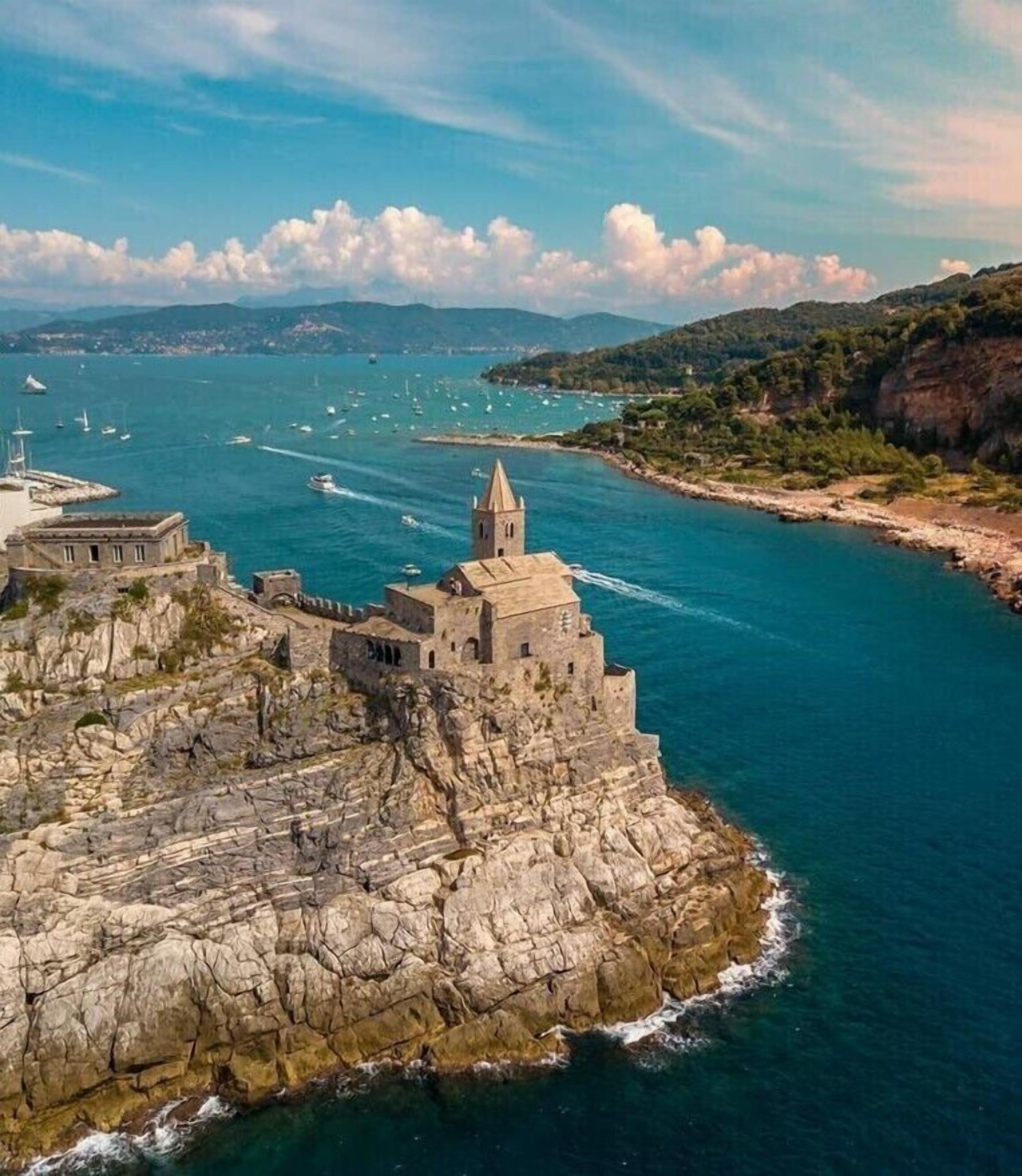 Un bâtiment en pierre situé sur la côte, doté d’une tour, et entouré d’un paysage rocheux et d’une mer d’un bleu limpide.