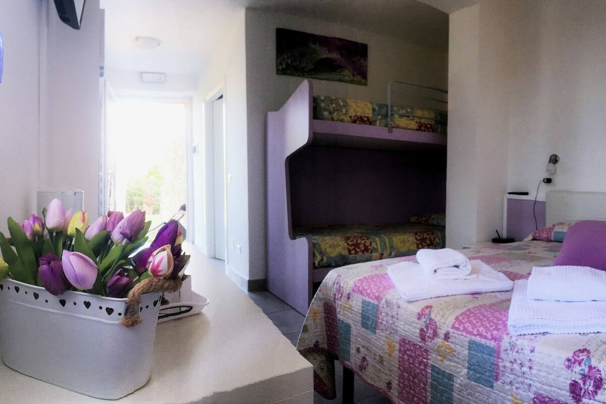 Una camera da letto con un letto a castello, un comodino, un tavolino di fianco al letto e un letto con copriletto, più un quadro appeso al muro.