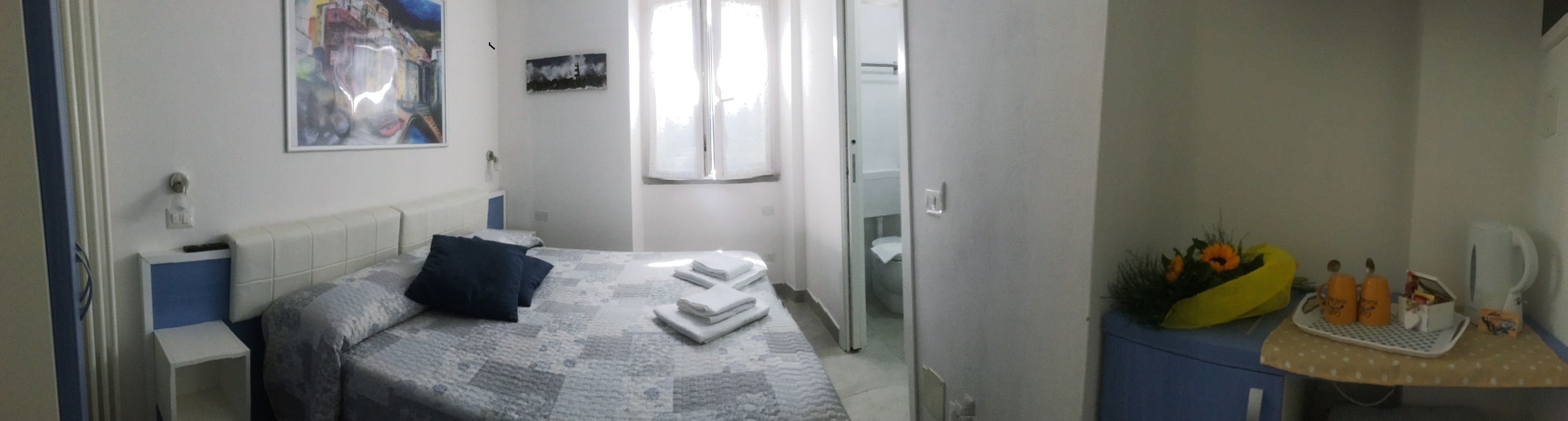 A bedroom with a bed, a bedside table, a mirror, a window, and a small desk with a chair.
