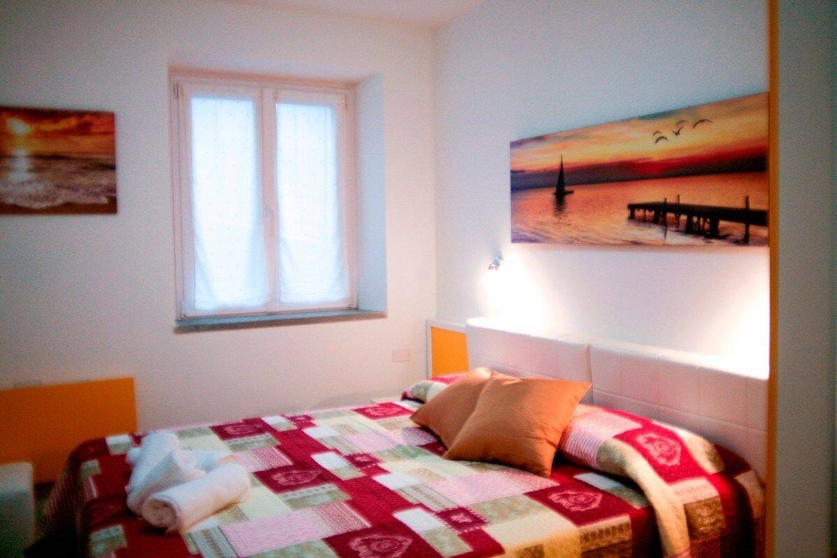 Una camera da letto con un letto, una finestra e un dipinto di un tramonto sull'acqua.