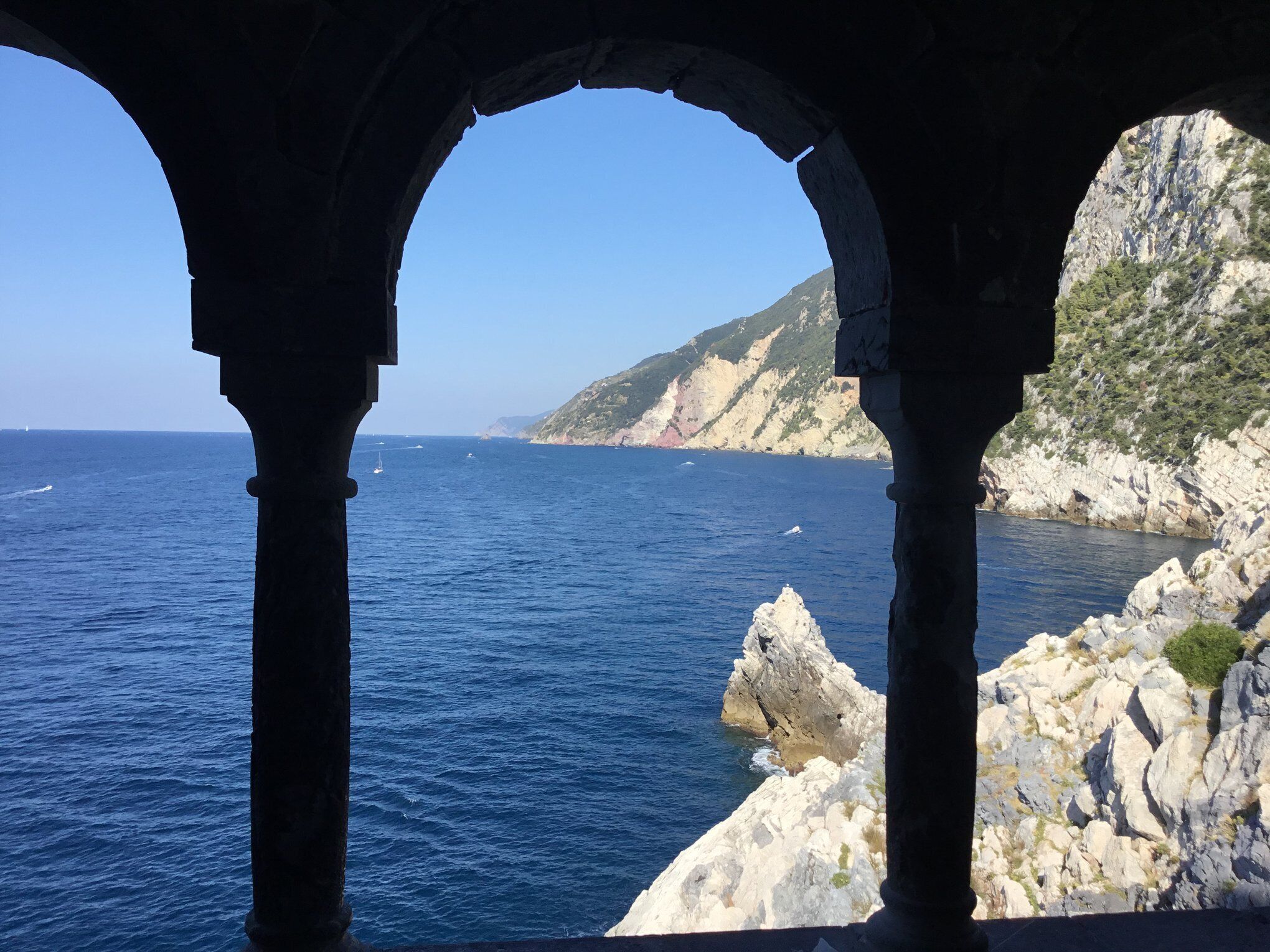 A coastal view through an arched stone structure with clear blue sea and rocky cliffs.