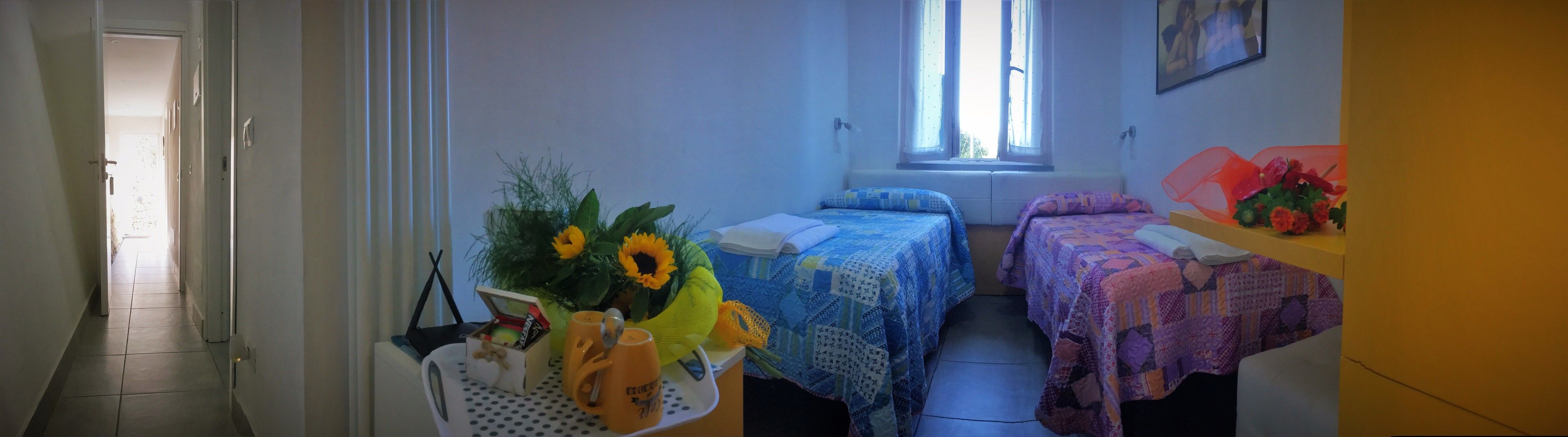 Una stanza piccola e luminosa con due letti, una finestra e un tavolo con un vaso di fiori.