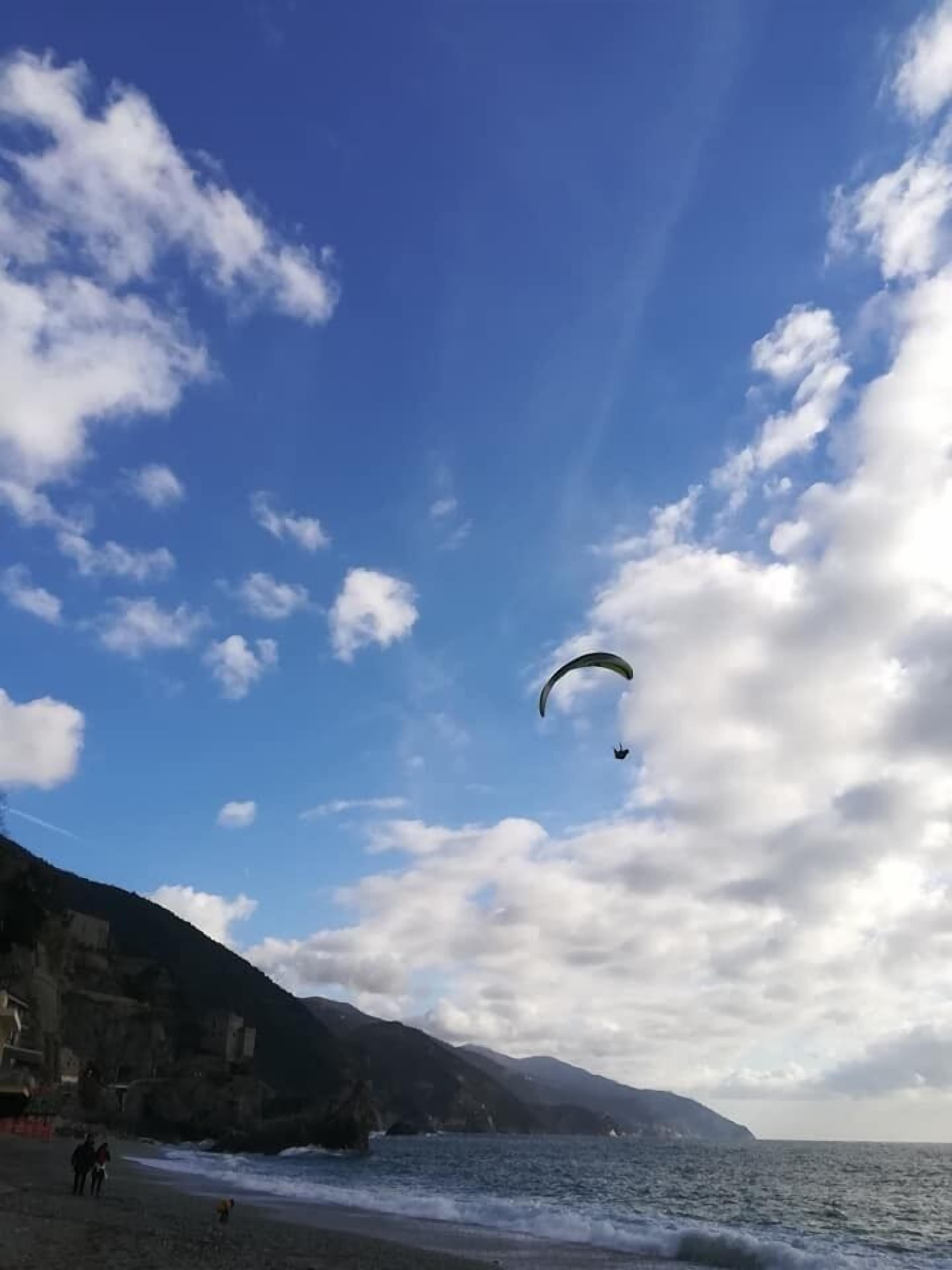 Una playa con una persona parapenteando, un litoral rocoso y olas rompiendo sobre la orilla.
