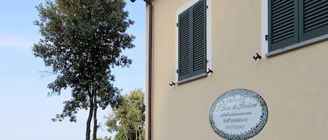 Un bâtiment orné d’une plaque, avec des volets verts et des fleurs roses au premier plan.