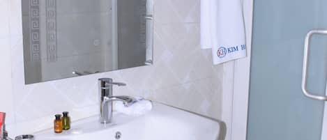 Ein Badezimmer mit Waschbecken, Spiegel und Dusche mit Milchglas-Tür.