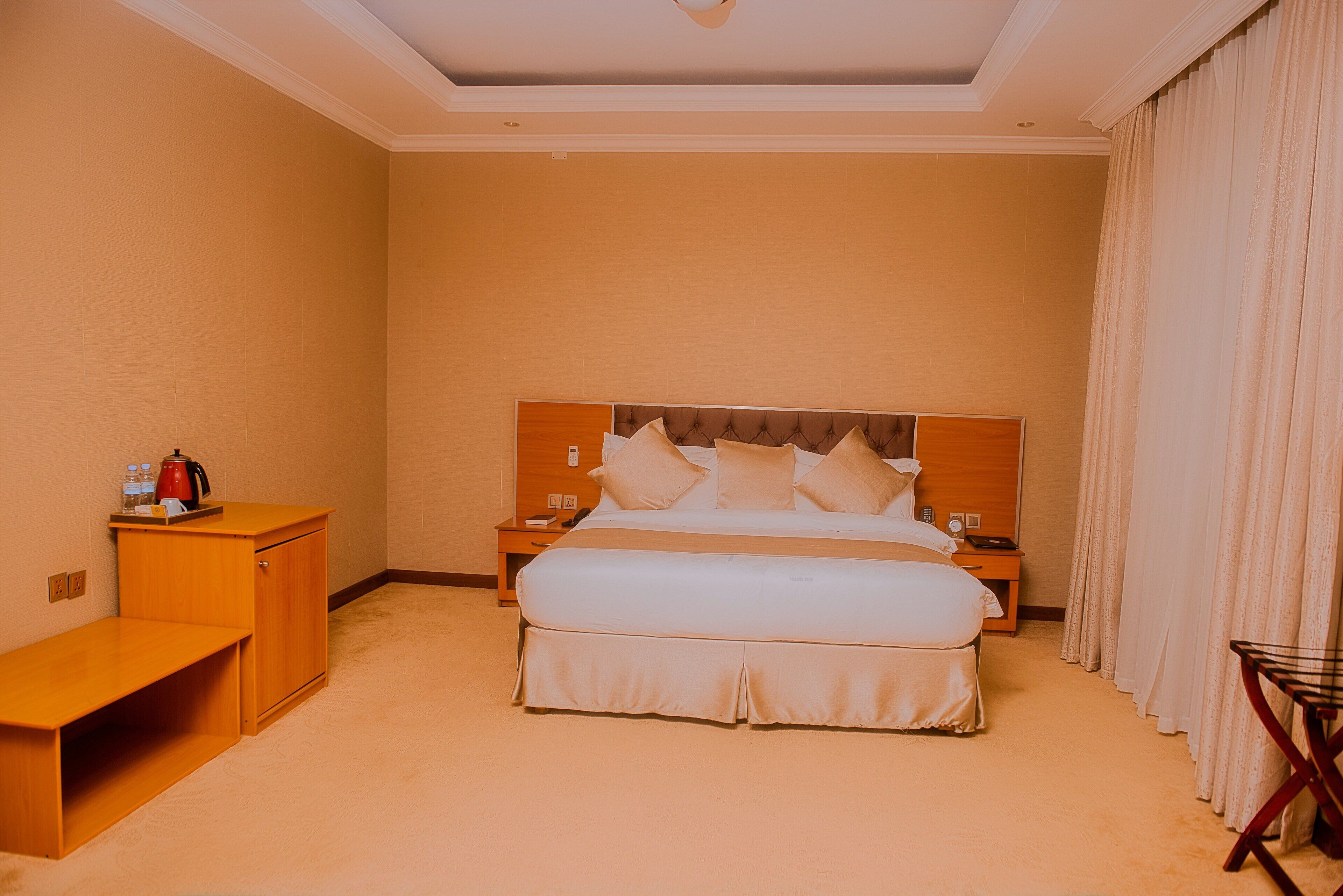 A hotel room with a large bed, bedside tables, a wooden bench, and a small table with a kettle.