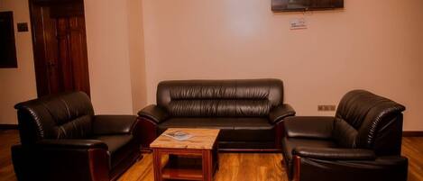 A living room with a black leather sofa, two armchairs, and a wooden coffee table.