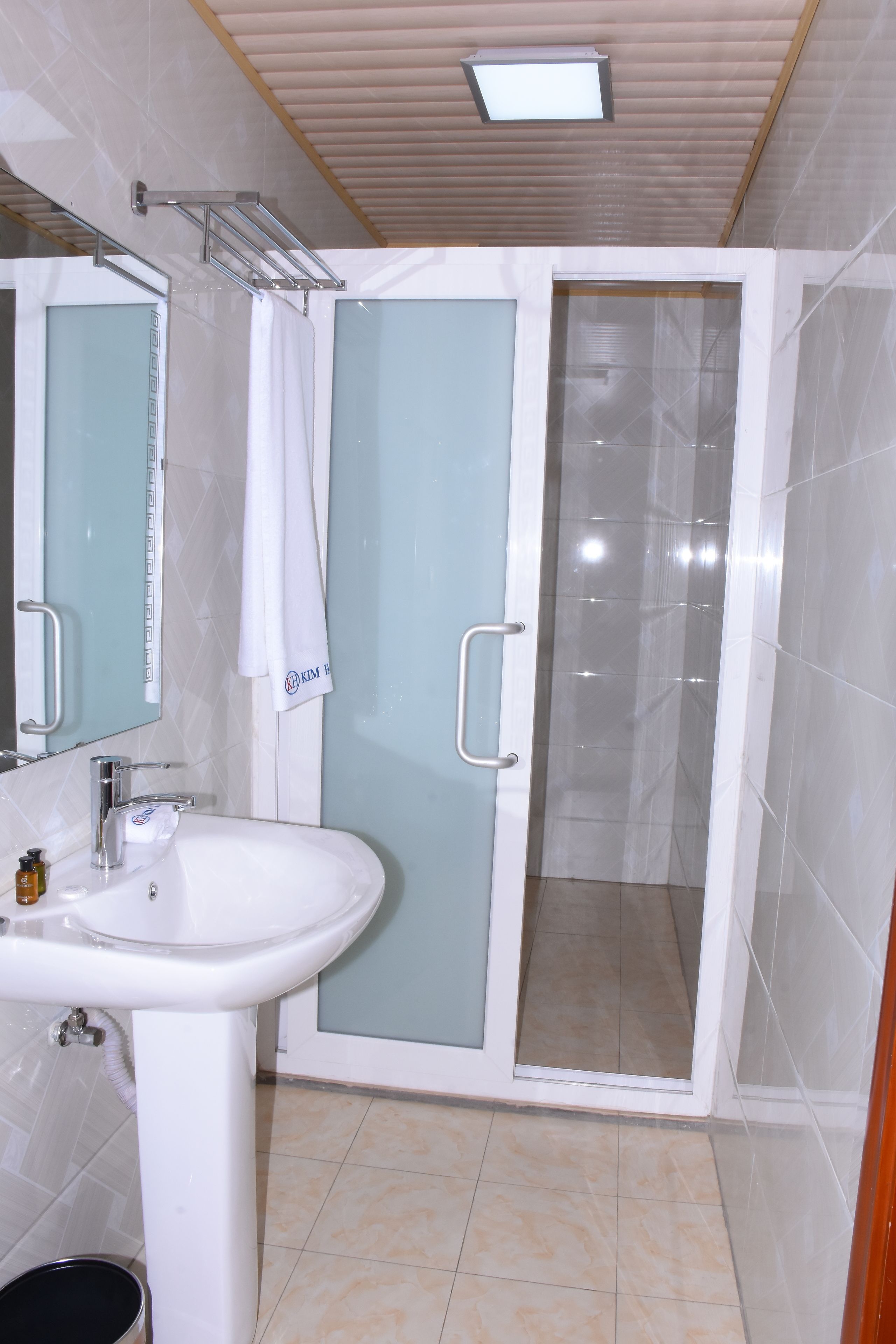 Un baño con un lavamanos blanco, una cabina de ducha de vidrio y un espejo con una toalla colgada.