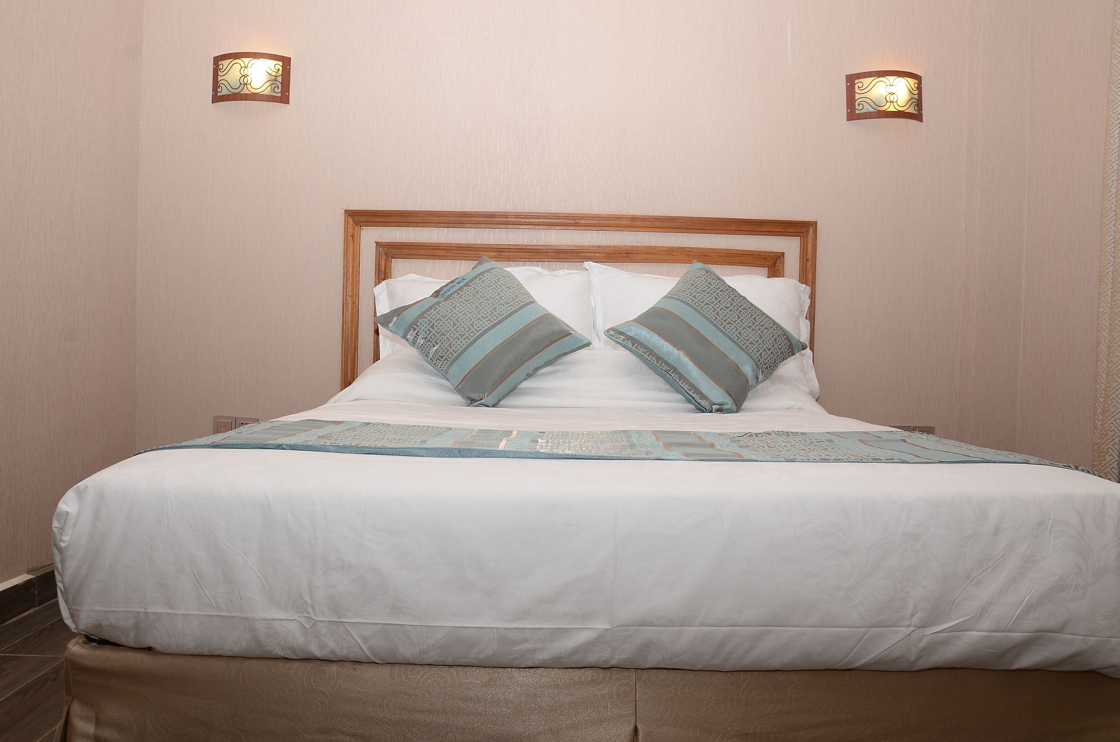 A neatly made bed with a wooden headboard, two decorative wall sconces, and a patterned throw blanket.