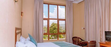 A hotel room with a large bed, a desk with a chair, a television, and a window with curtains.