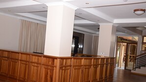 A spacious lobby with a wooden reception desk, high ceilings, and a view of the outdoor area.