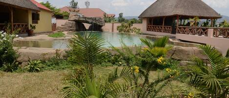 Un resort con piscina, estructuras de techo de paja y exuberante vegetación.