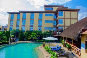 A hotel with a swimming pool, a thatched-roof structure, and a multi-story building with large windows. - KIM Hotel (Kigali)