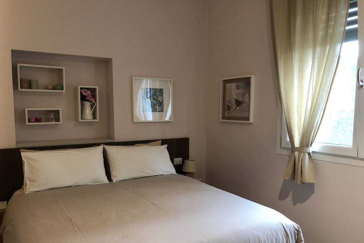A neatly made bed with white linens, a bedside table with a lamp, and wall-mounted shelves with decorative items.