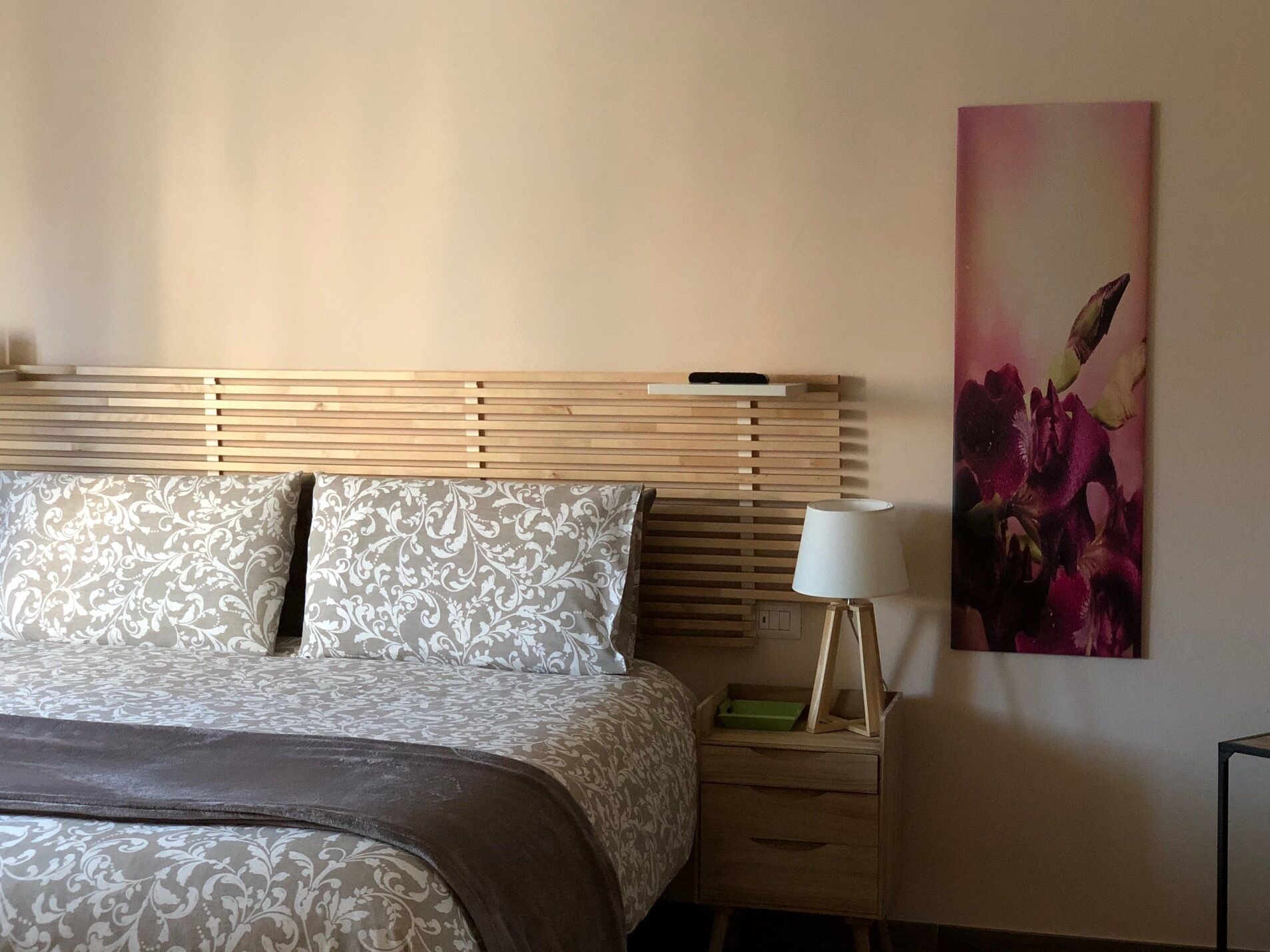 Una cama bien hecha con ropa de cama estampada, una mesita de noche con lámpara y una obra de arte colgada en la pared.