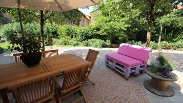 Un patio exterior con una mesa y sillas de madera, un sofá rosa y plantas en macetas.