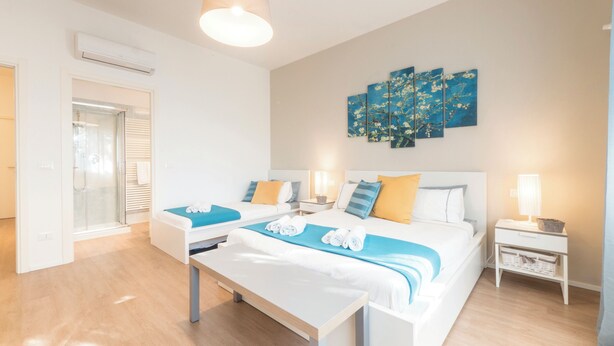 A hotel room with two beds, a bench, a wall-mounted artwork, and a bedside table with a lamp. - VILLA DUE GIARDINI (Padova)