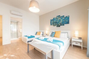 Une chambre d’hôtel avec deux lits, un banc, une œuvre d’art accrochée au mur et une table de chevet avec une lampe.