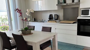 A modern kitchen with white cabinets, a dining table with chairs, a coffee maker, and a microwave. - VILLA DUE GIARDINI (Padova)