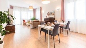 A spacious living area with a dining table, chairs, a sofa, and a coffee table. There is a large plant and a painting on the wall. - VILLA DUE GIARDINI (Padova)