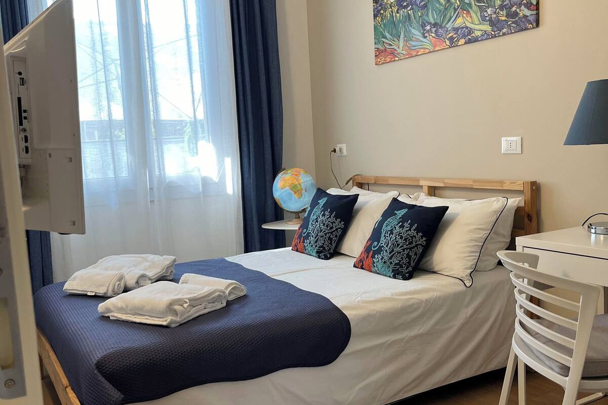 A hotel room with a bed, a desk, a chair, a globe, and a painting on the wall.