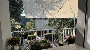 A balcony with a view of a garden, a white railing, and a beige umbrella. - VILLA DUE GIARDINI (Padova)