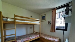 Habitación con literas de madera, una escalera pequeña, un estante y una ventana con cortinas.