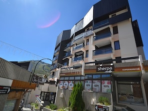 A multi-story building with a supermarket named 'Sherpa' on the ground floor, a restaurant named 'Class Restaurant' on the second floor, and a sign for 'ABSOLU SPORTS' indicating a ski rental location.