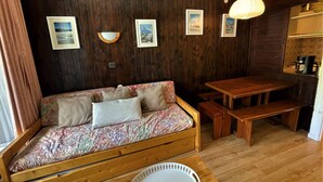 Una habitación acogedora con un sofá y una mesa de madera, además de un banco. Se observan cuadros en la pared y una lámpara colgante.
