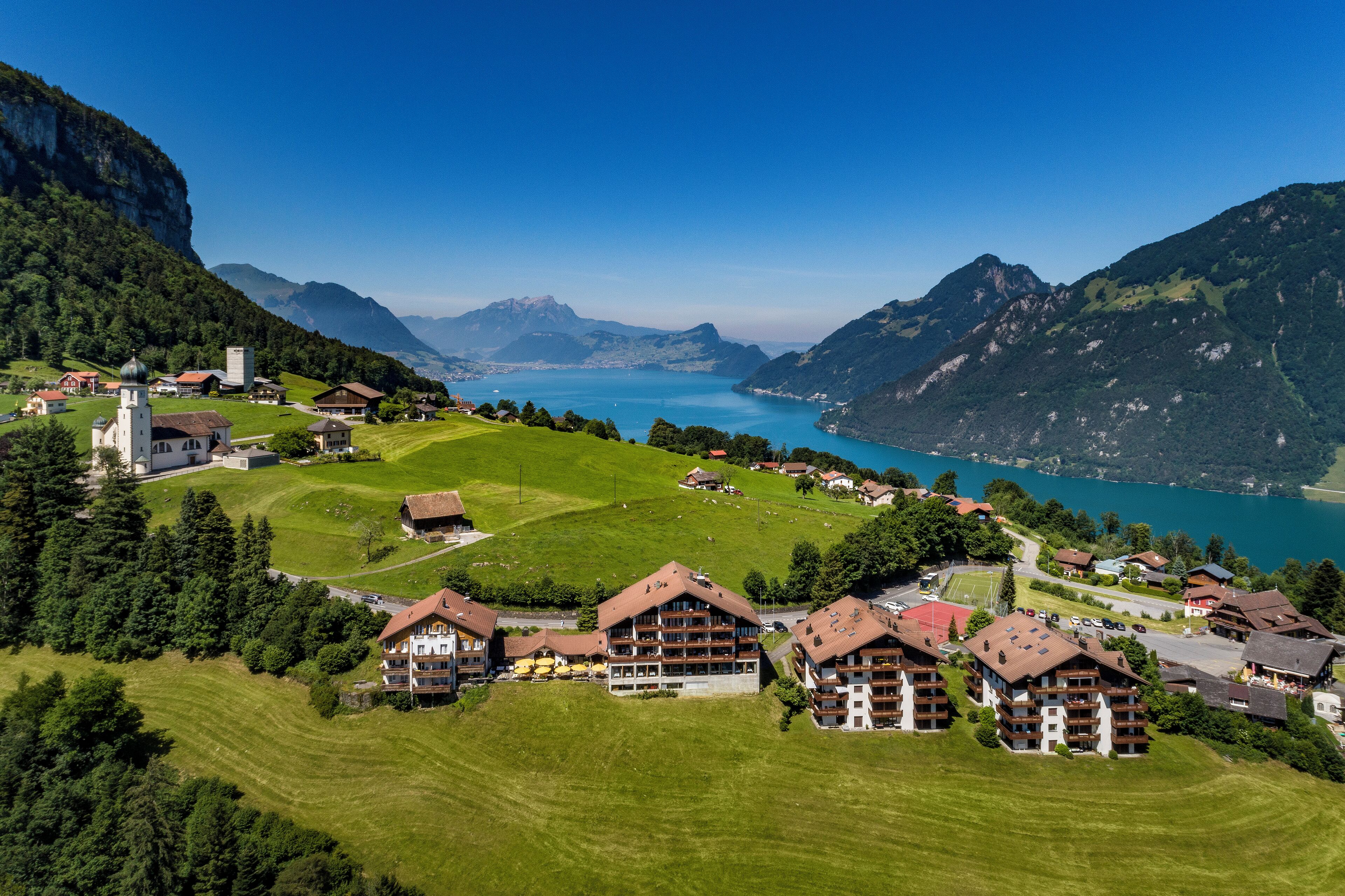 A mountainous village with traditional buildings, a church, and a lake.