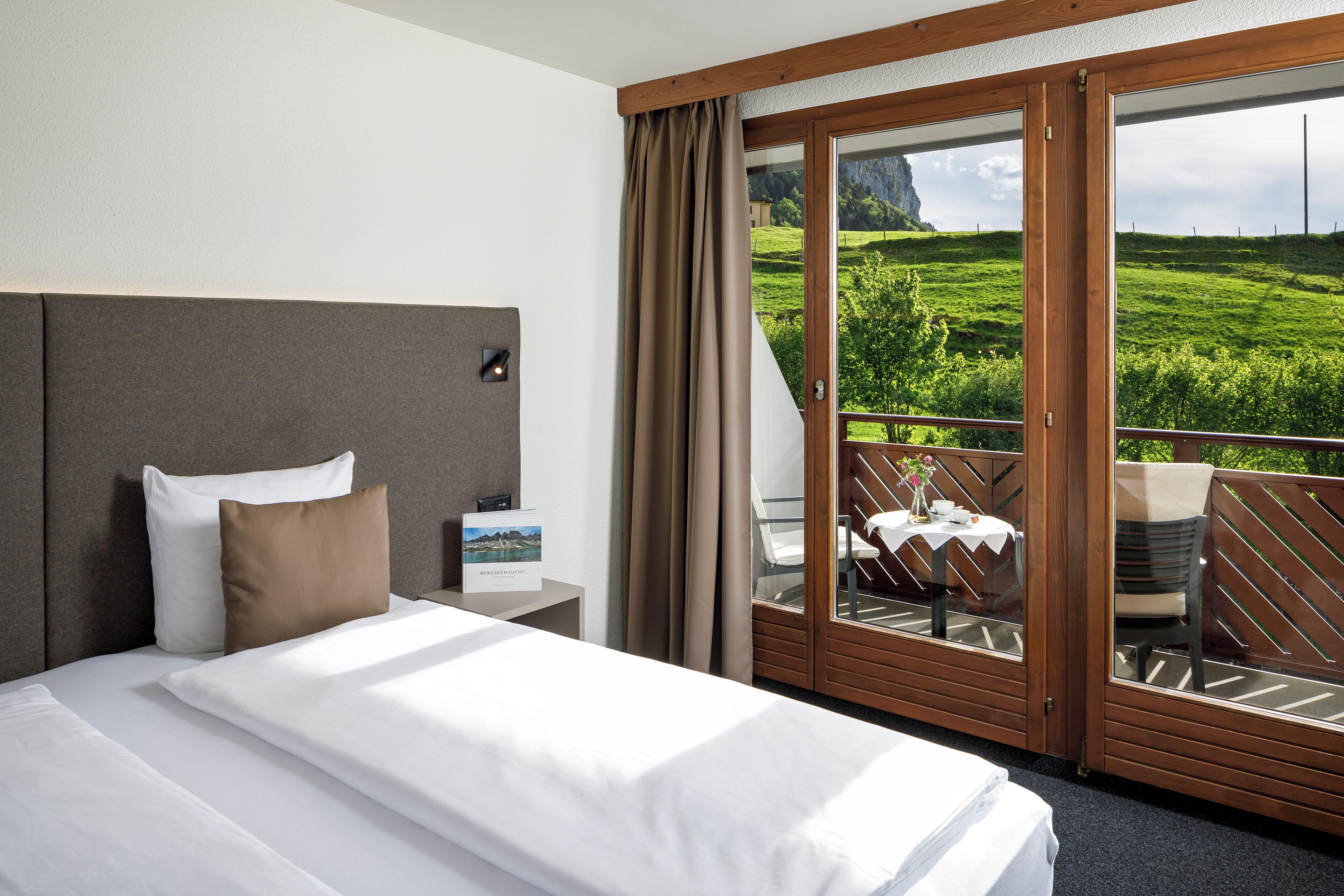 Hotelkamer met een bed, nachtkastje, uitzicht op een balkon met tafel en stoelen en een prachtig buitengezicht.