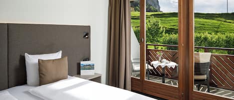 A hotel room with a bed, a nightstand, a view of a balcony with a table and chairs, and a scenic outdoor view.
