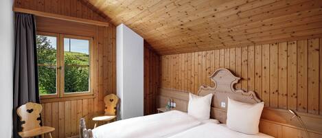 A wooden-paneled room with a double bed, a chair, a bedside table, and a window with a view of greenery.