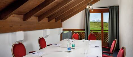 A conference room with a white table, red chairs, and a view of a grassy landscape through large windows.