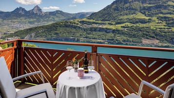 A terrace with a table set for two, overlooking a mountainous landscape and a lake.