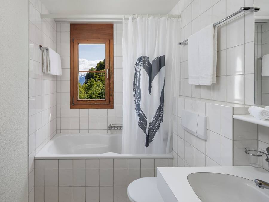 A modern bathroom with a bathtub, a window with a view of greenery, and a white sink with a mirror.