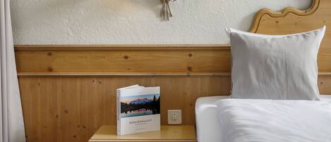 A neatly made bed with white linens, a wooden headboard, and a bedside table with a book titled "BERGEENSUCHT".