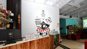A reception desk with a 'MEET YOU' sign, a wooden counter, and a wall with shelves and various items. - Meet int'l Youth Hostel Zhejiang Rd (Qingdao)