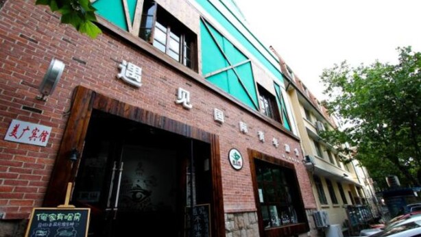A building with a brick facade and a green awning. There is a sign with Chinese characters and a logo on the wall. - Meet int'l Youth Hostel Zhejiang Rd (Qingdao)