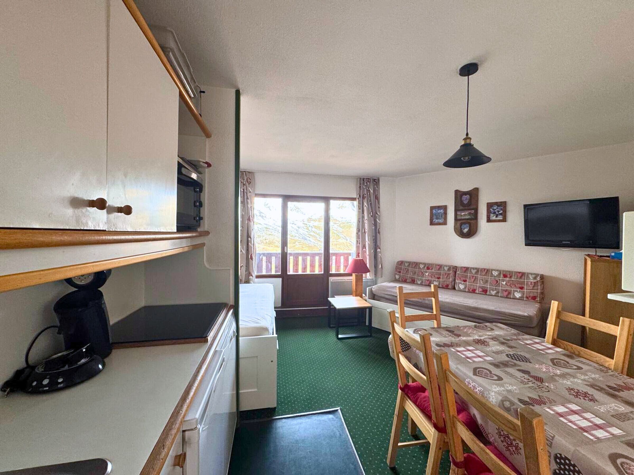 A compact room with a kitchenette, a sofa, a dining table, and a TV.