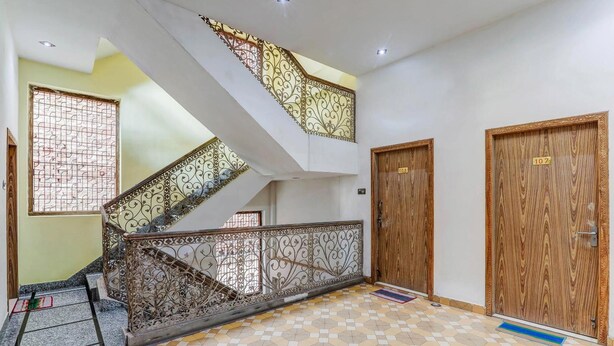 Un vestíbulo de hotel con un suelo de diseño geométrico, una escalera con barandillas de metal ornamentadas y puertas de madera con números de habitación.