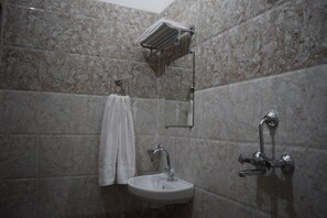 A bathroom with a marble wall, a sink, a towel rack, and a shower head. - Hotel KV Palace (Varanasi)