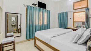 Un dormitorio con cama, mesita de noche, espejo, ventana con cortinas y un baño visible a través de una puerta abierta.